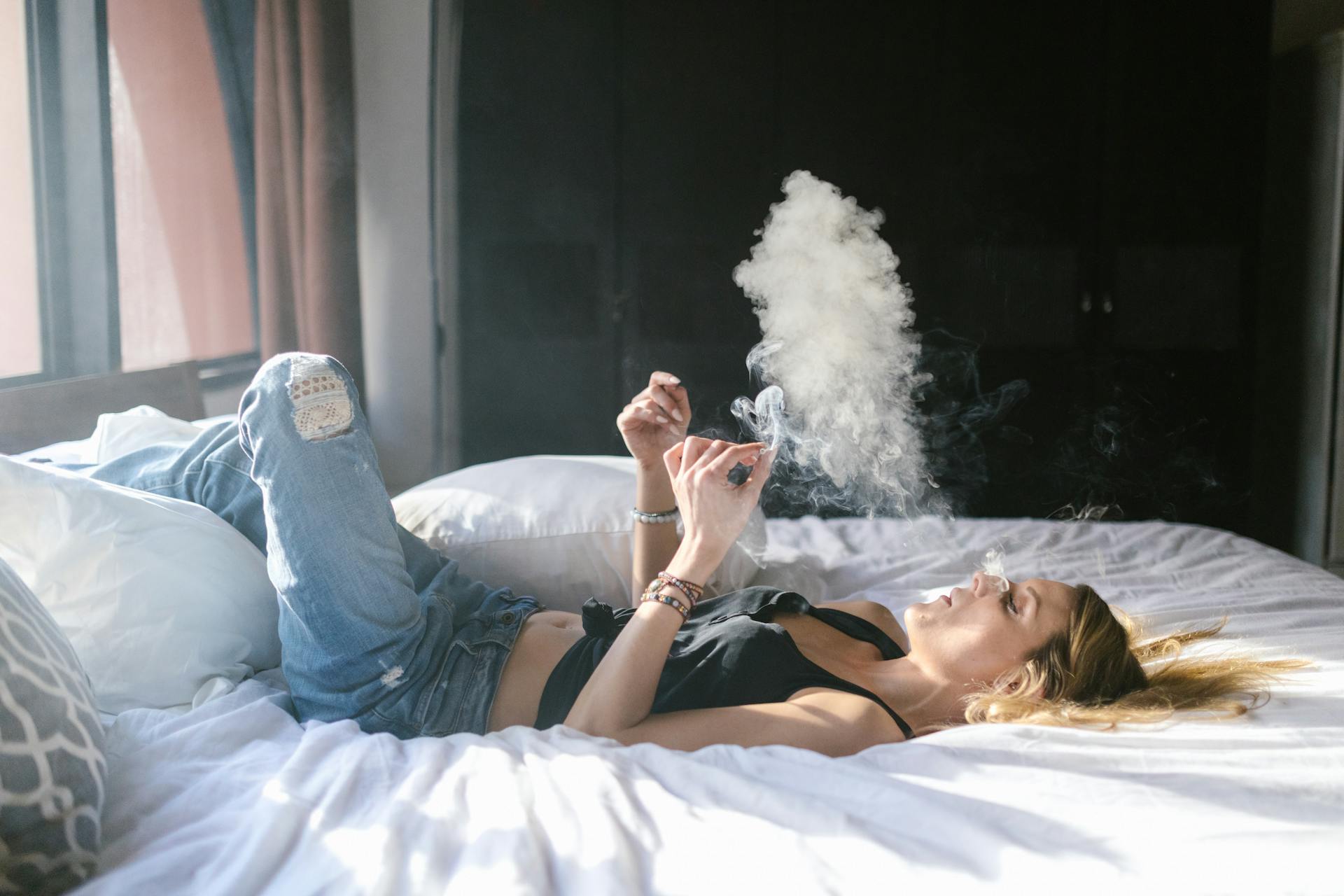 A woman lying in bed smoking weed