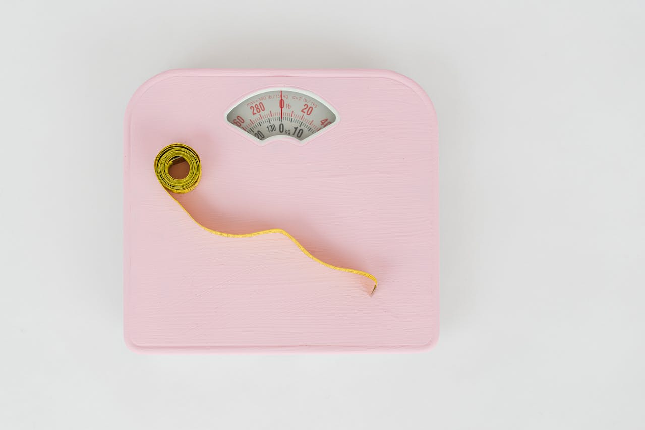 Pink scale and yellow tape measure on a white floor